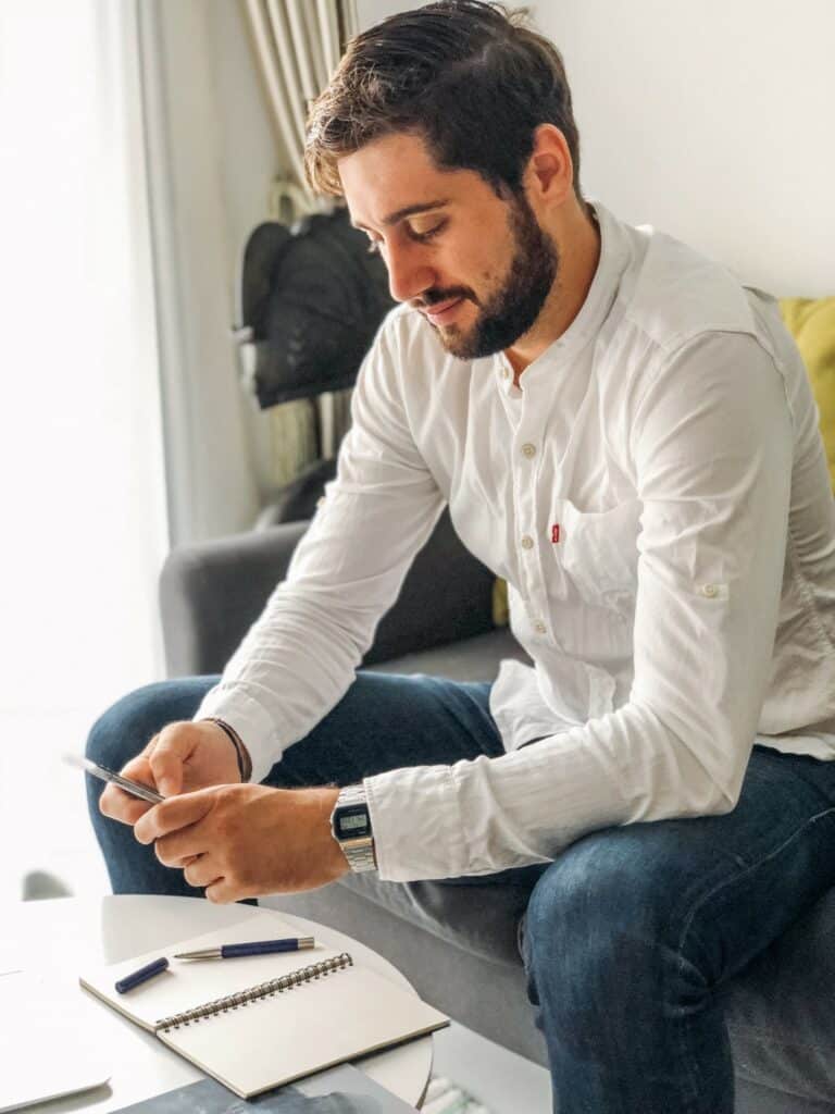 Young millennial with a beard browsing his phone on a sofa